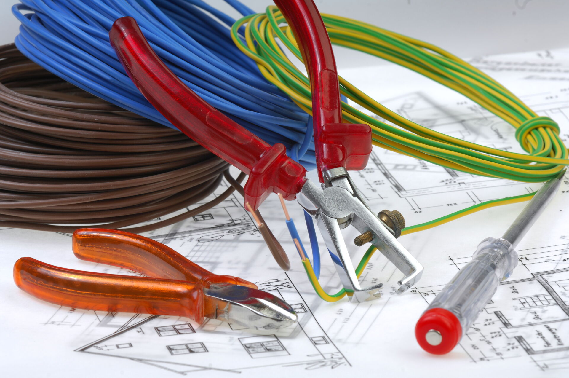 Elektroinstallationswerkzeug wie Zangen, Abisolierer, Schraubendreher und Kabel auf Bauplänen. Elektro Bohr in Saalfeld.
