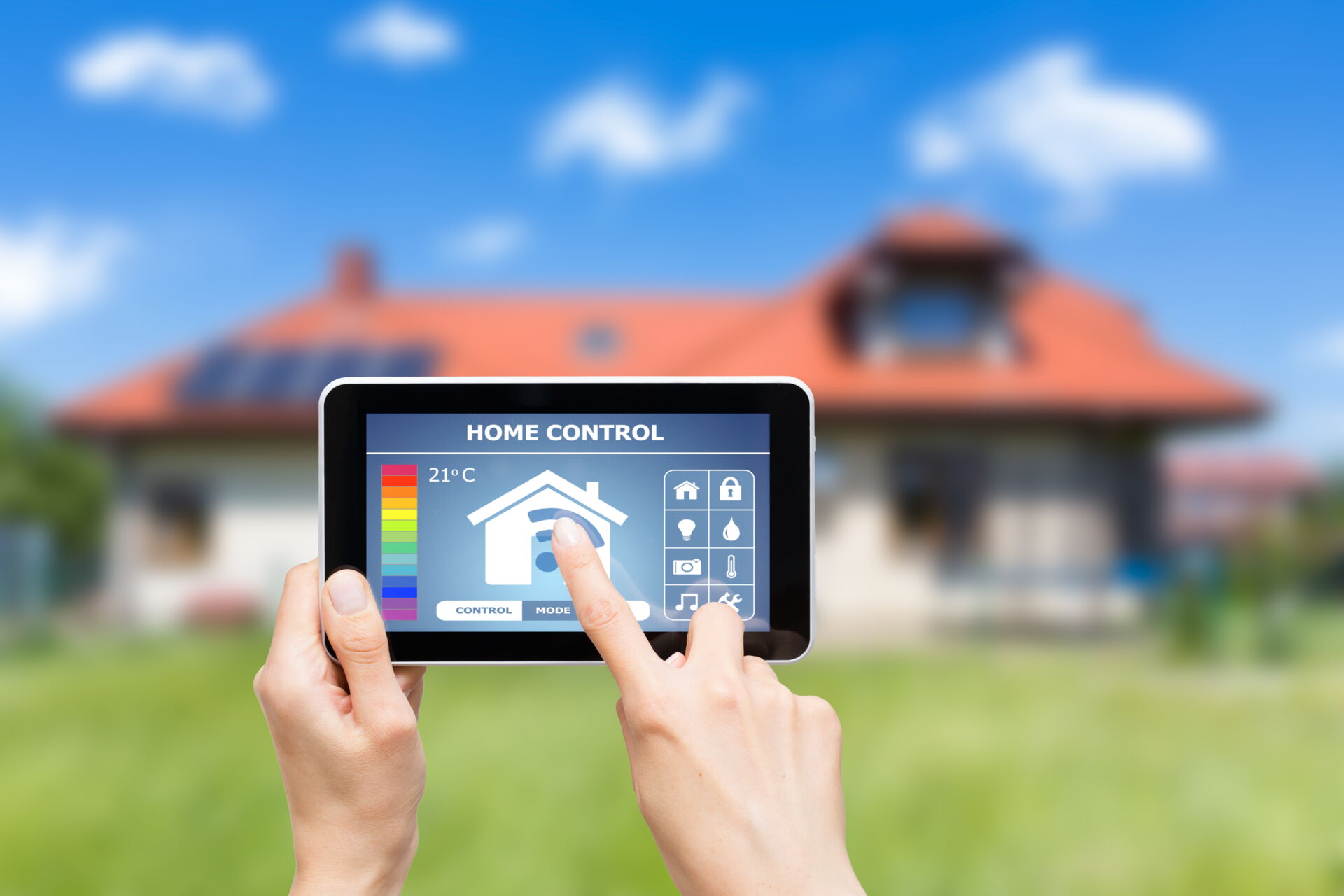 Ein Tablet mit Smart-Home-Steuerung wird vor einem unscharfen Haus mit Solaranlage bedient. Elektro Bohr in Saalfeld.