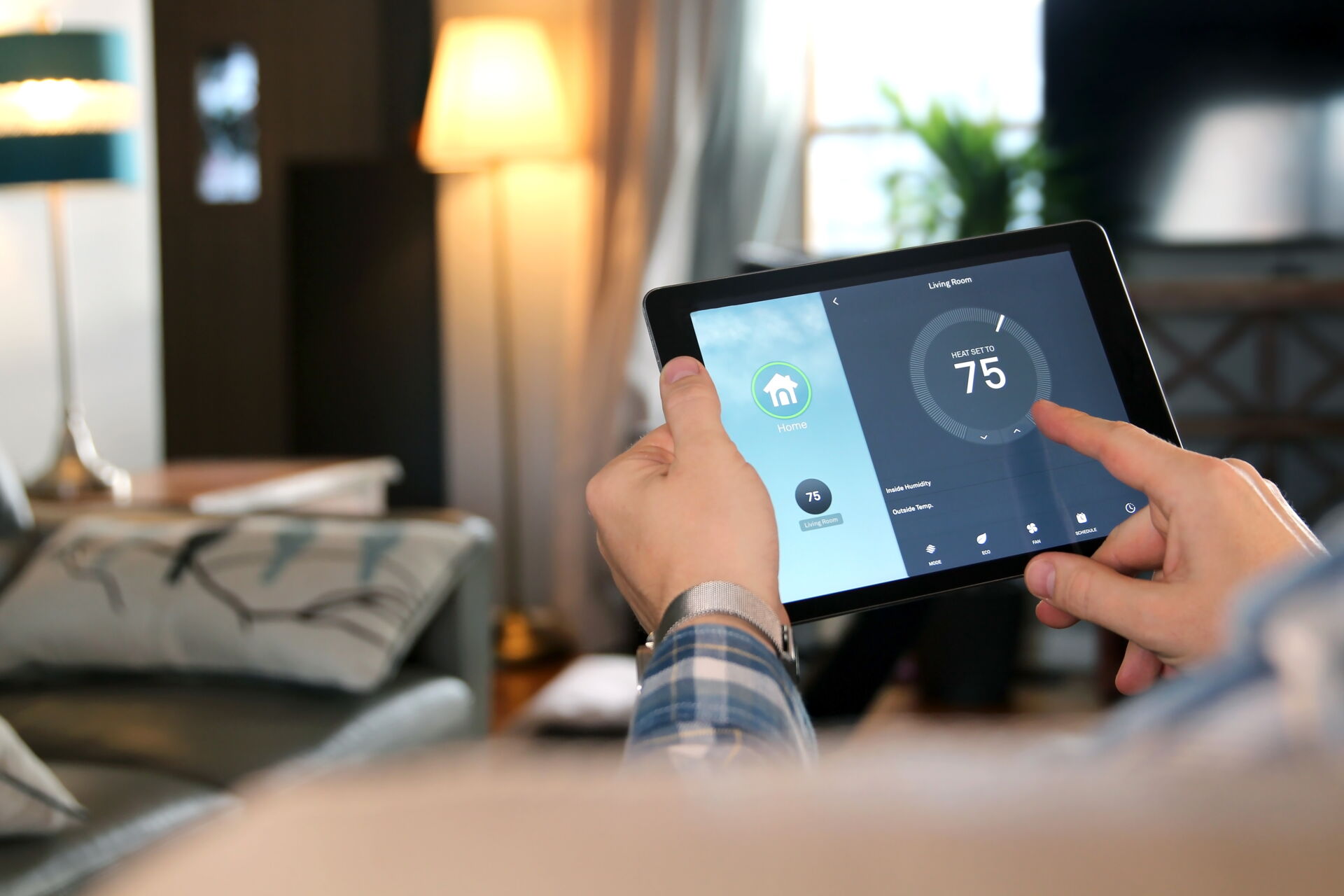 Hände bedienen ein Tablet zur Steuerung eines intelligenten Thermostats im Wohnzimmer. Elektro Bohr in Saalfeld.