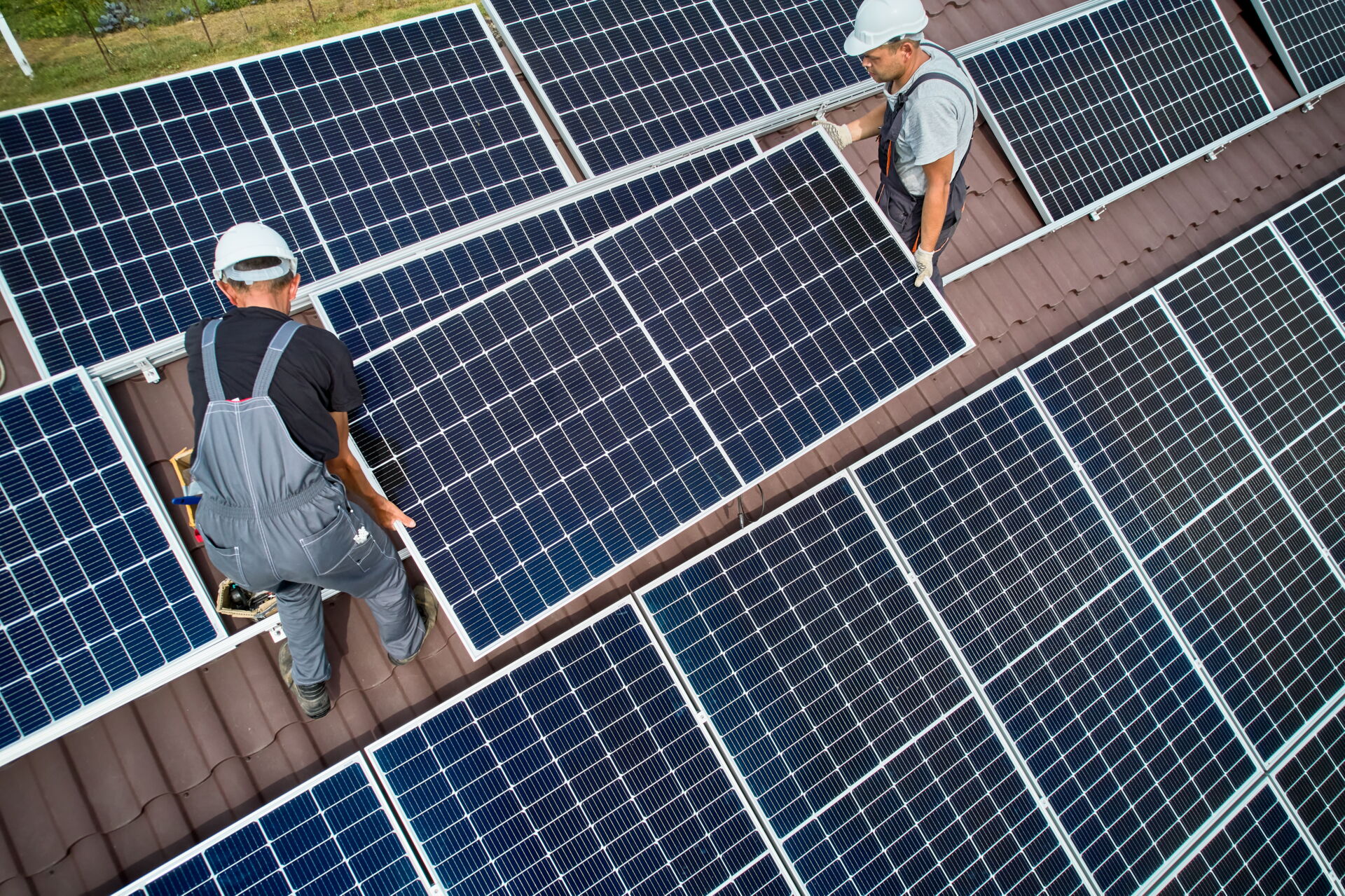 Zwei Handwerker in Arbeitskleidung installieren Solarmodule auf einem Dach. Elektro Bohr - Ihr Handwerksbetrieb in Saalfeld.