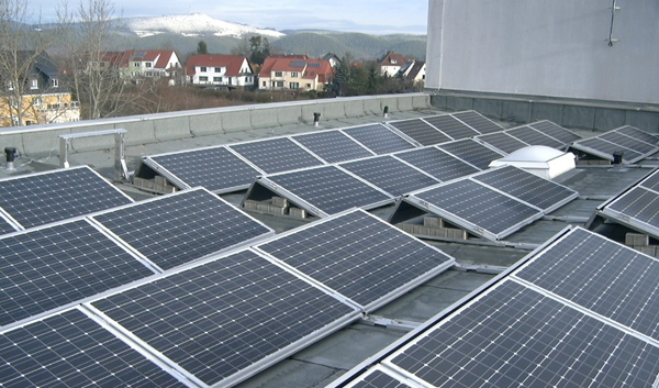 Eine Photovoltaikanlage auf einem Dach mit Blick auf eine Stadt und bewaldete Hügel. Elektro Bohr in Saalfeld.